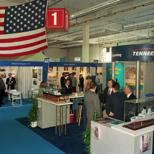 inige Messestände mit Besuchern; an der Decke wurde eine USA-Flagge aufgehängt