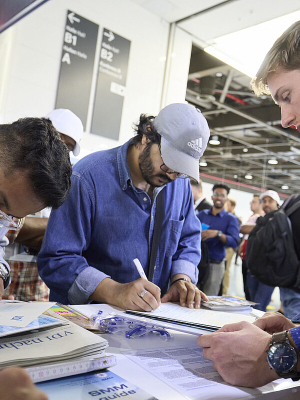 Mehrere Ausstellende stehen an einem Pult und füllen ein Papier aus. 