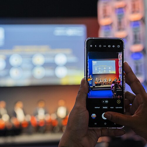 eine Aufnahme eines Smartphones, welches ein Bild von der Bühne macht. 