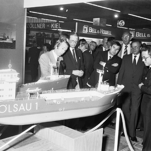 Mehrere Messebesucher, die sich das Miniaturschiff "Öslau 1" anschauen. Im Hintergrund sind weitere Messestände zu sehen.