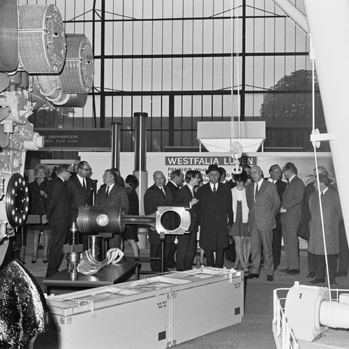 Historisches Bild einer Gruppe von Messebesuchern, die sich große, hier im Vordergrund stehende, Schiffsteile anschauen.