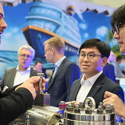 Aufnahme von einem Austeller und zwei Besucher im Gespräch. 