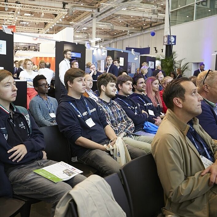 Menschen, die in mehreren Reihen im Publikum sitzen und zuhören. 