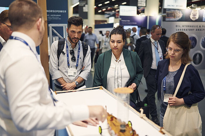 Drei Besuchende unterhalten sich mit Ausstellenden.