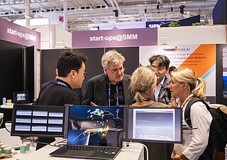 Ausstellende und Besucher unterhalten sich im Start-up Bereich. Es sind einige Bildschirme zu sehen. 