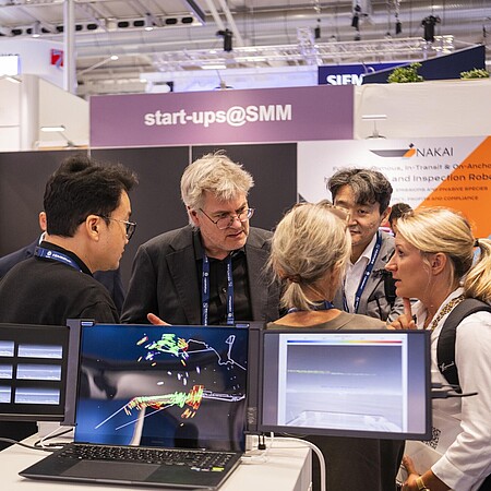 Ausstellende und Besucher unterhalten sich im Start-up Bereich. Es sind einige Bildschirme zu sehen. 